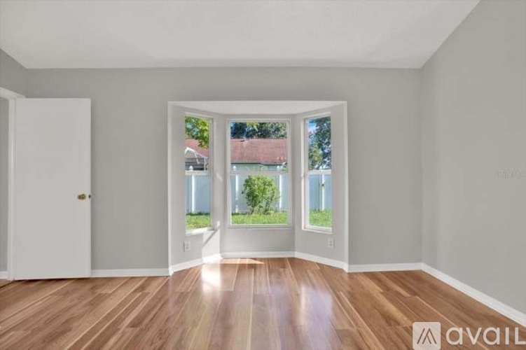 A spacious room with wooden floors and a view of the outdoors through the windows.