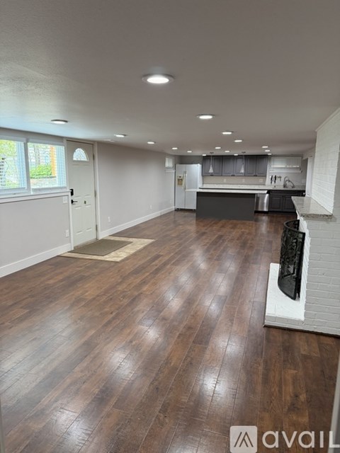 A room with wooden flooring and a kitchen area in the background.