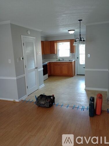A room with wooden floors and a kitchen area in the background.