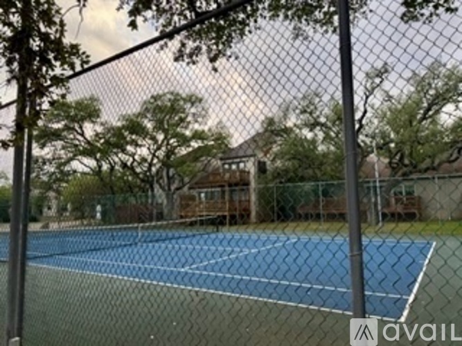 A tennis court is surrounded by a fence and trees.