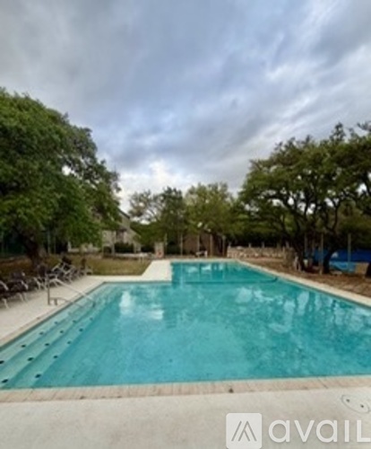 A swimming pool surrounded by trees and a cloudy sky.