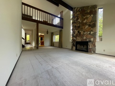 A spacious living room with a stone fireplace and a balcony.