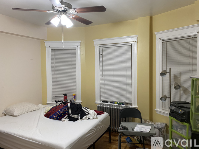 A bedroom with a bed, desk, and window with blinds.