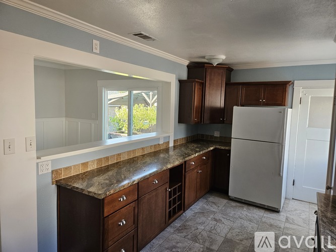 A kitchen with a refrigerator, cabinets, and a window.