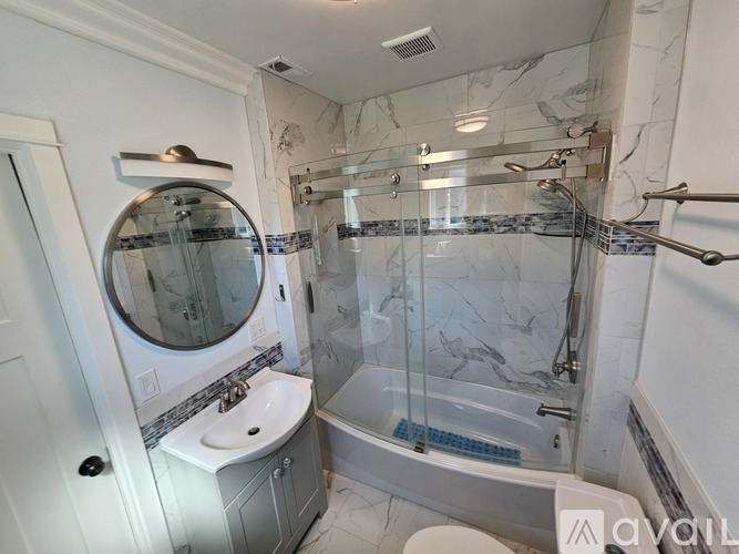 A white bathroom with a marble shower and a glass door.