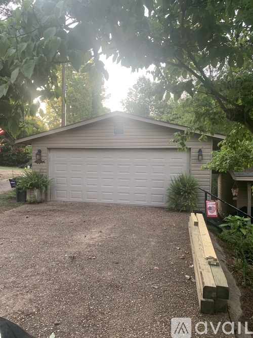 A garage with a white door is surrounded by trees and has a bench in front of it.