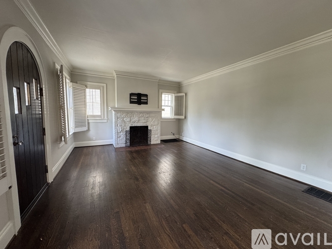 A spacious room with a fireplace and dark wood flooring.