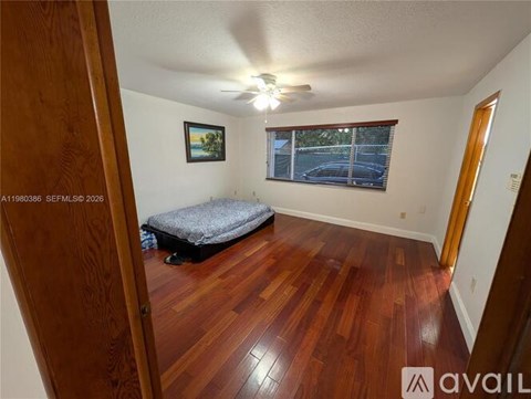 A bedroom with a bed, wooden floors, and a window with blinds.