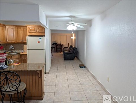 A kitchen with a refrigerator, a dining table with chairs, and a living room with a couch.