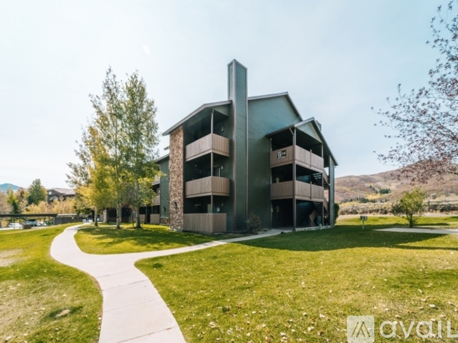 A modern building with a curved facade and balconies is surrounded by a grassy area and trees.