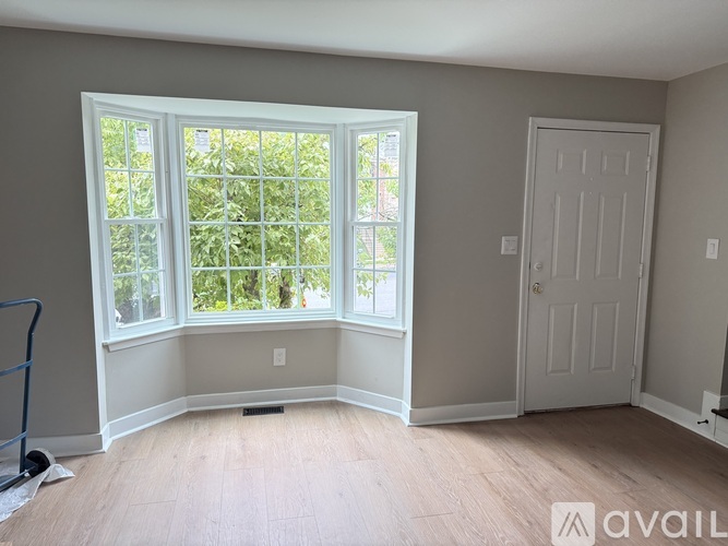 A room with a white door and a window with a view of trees.