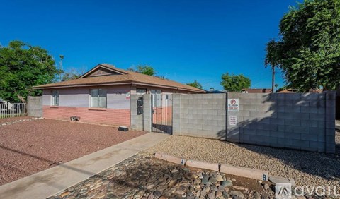 A house with a brown roof and a grey wall with a gate in front.