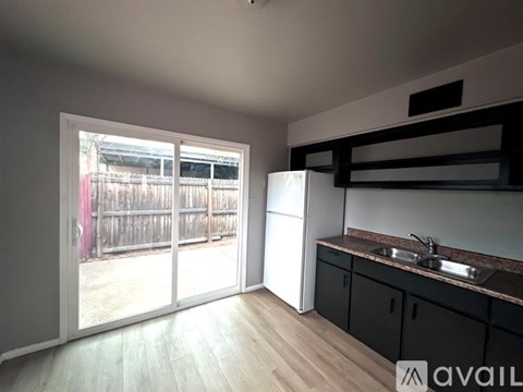 A kitchen with a sink and a refrigerator with a window overlooking a backyard.