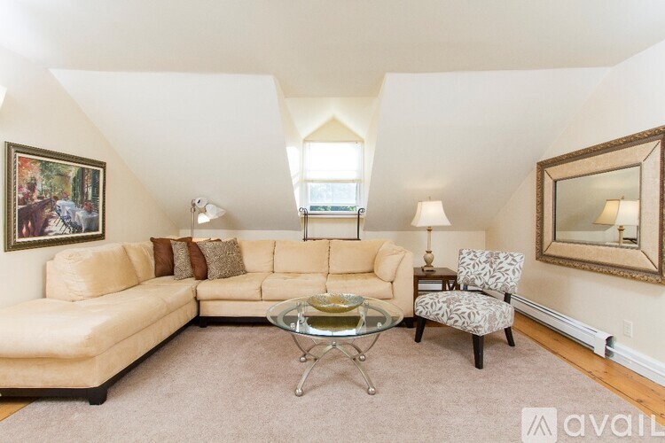 A living room with a tan couch, a glass coffee table, and a chair with a patterned cushion.