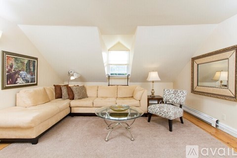 A living room with a tan couch, a glass coffee table, and a chair with a patterned cushion.
