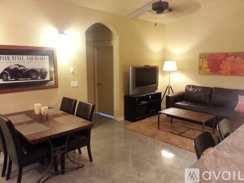A living room with a brown leather couch, a wooden dining table with chairs, a television, and a painting on the wall.