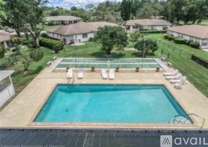 A swimming pool surrounded by a grassy area and a tennis court.