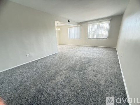 A spacious room with grey carpeting and two windows.