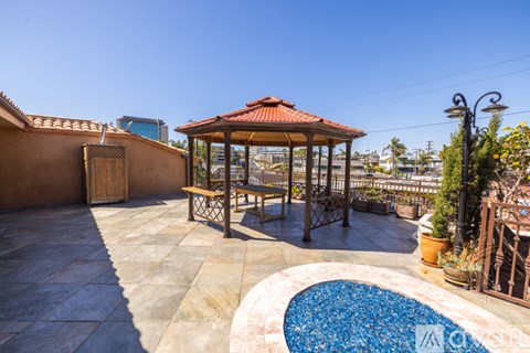 A gazebo with a table and chairs is surrounded by a pool and plants.