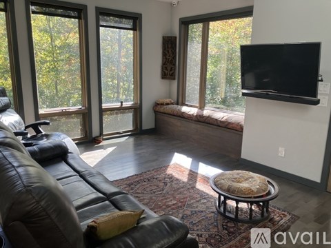 A living room with a black leather couch and a flat screen TV mounted on the wall.