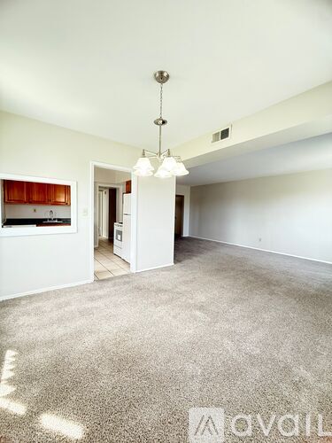A spacious living room with a carpeted floor and a chandelier hanging from the ceiling.