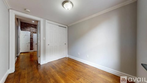 A room with wooden floors and white walls, with a doorway leading to another room.