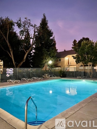 A pool surrounded by trees and chairs at dusk.