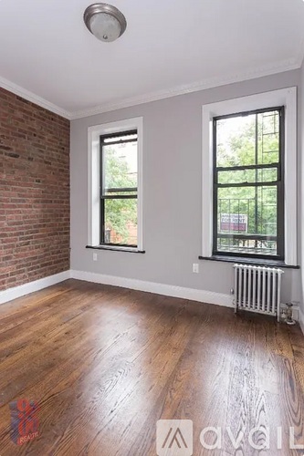A room with a wooden floor and a brick wall with two windows.
