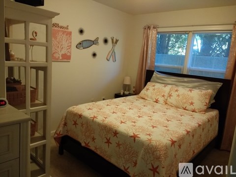 A bedroom with a bed, a nightstand, a window with curtains, and a wall decorated with a fish and a pair of scissors.