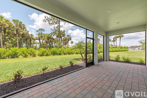 A patio area with a brick floor and a view of a green lawn and trees.