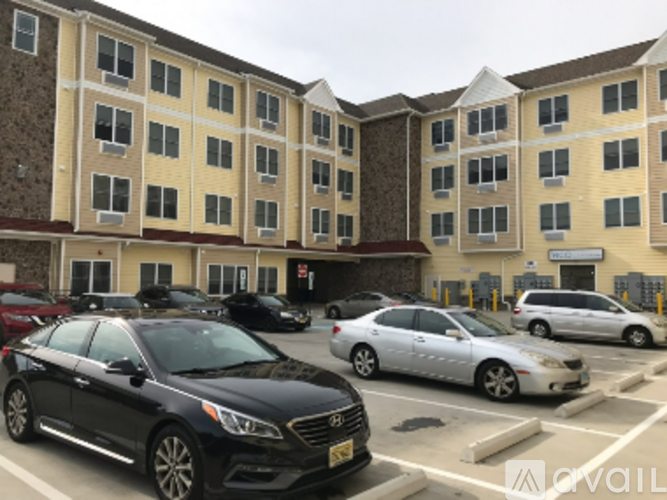 A black car is parked in a parking lot in front of a multi-story apartment building.