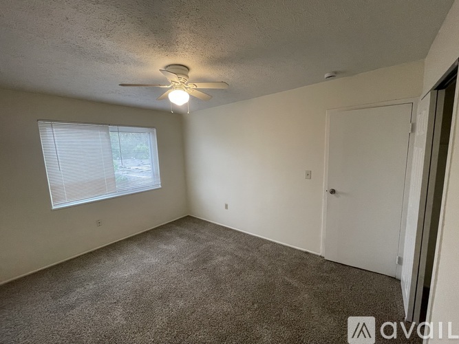 A room with a carpeted floor, a ceiling fan, and a window with blinds.