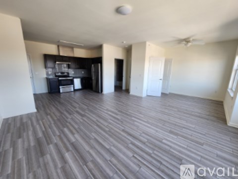 A spacious room with a wood floor and a kitchen area in the background.