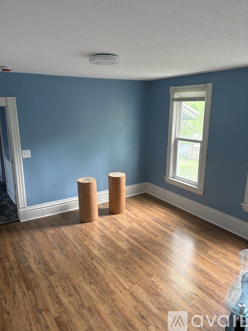 A room with blue walls and wooden floors has two cylindrical objects on the floor.