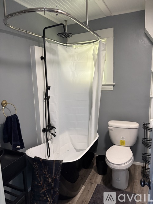 A bathroom with a toilet, a bathtub with a shower head and a towel hanging on the side.