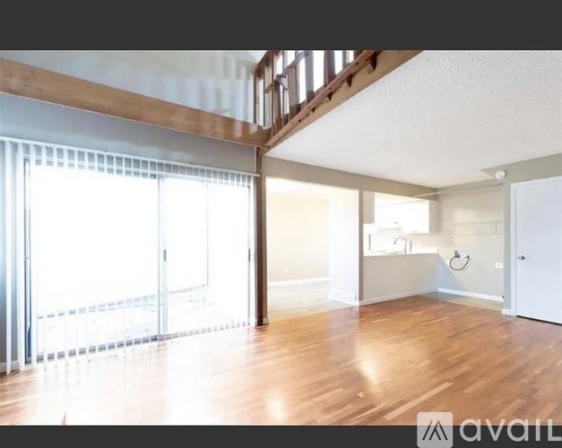 A spacious room with wooden floors and a staircase leading to the upper level.