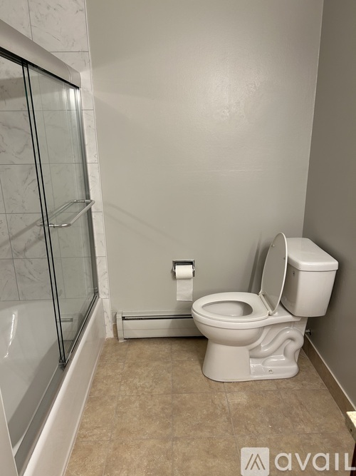 A white toilet with a toilet paper holder and a glass shower stall in a bathroom.