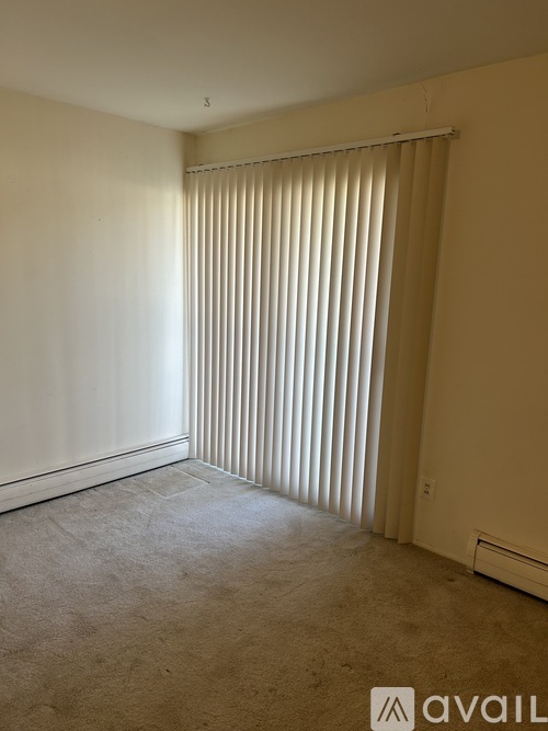 A room with a carpeted floor and a window with vertical blinds.