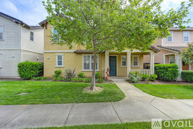A tree in front of a house with a green lawn.