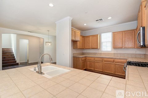 A large, empty kitchen with wooden cabinets and a stainless steel refrigerator.