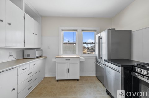 A kitchen with white cabinets and appliances, a window, and a tiled floor.
