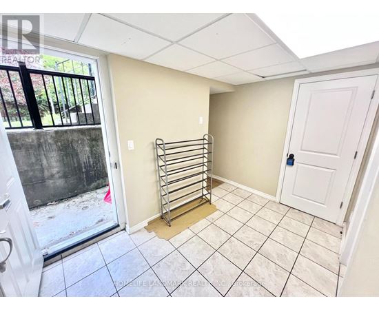 A room with a white door, a window with a view of a fence and trees, and a tiled floor.
