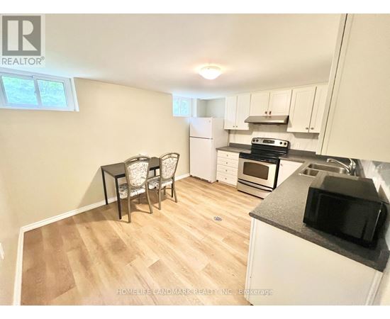 A kitchen with a table and chairs in the foreground and a refrigerator, microwave, oven, and stove in the background.