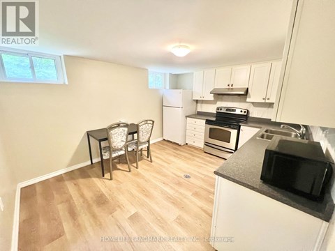 A kitchen with a table and chairs in the foreground and a refrigerator, microwave, oven, and stove in the background.
