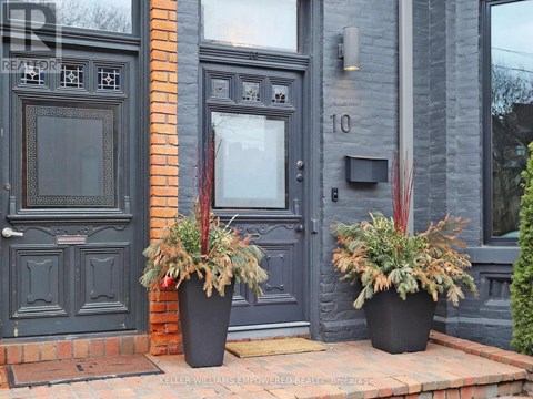 Two potted plants sit on a brick ledge in front of a black door.