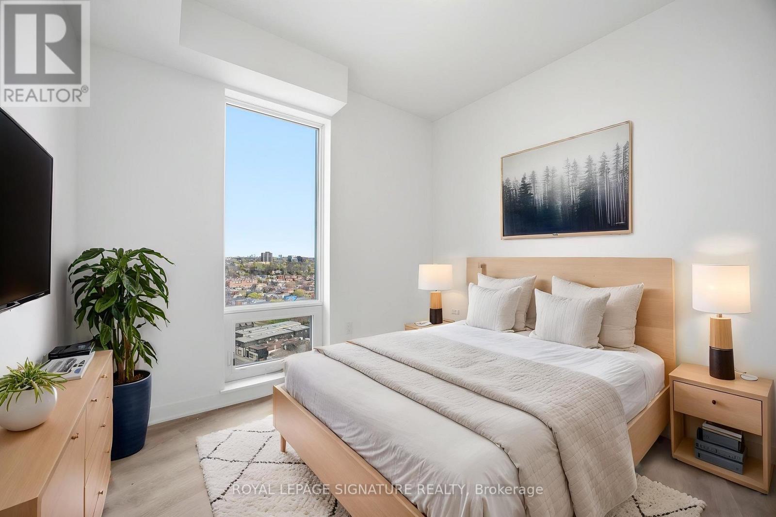 A bedroom with a large bed, a potted plant, and a painting on the wall.
