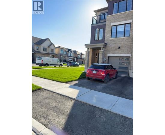 A red car is parked in front of a house with a white van in the background.