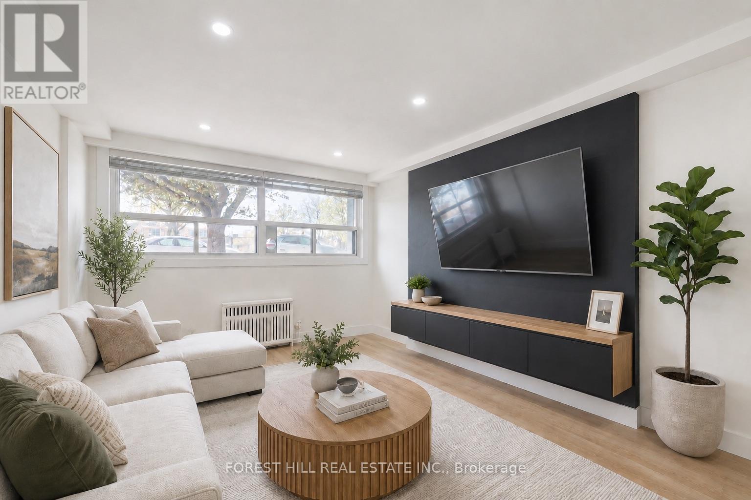 A modern living room with a white sofa, a wooden coffee table, and a flat-screen TV mounted on the wall.