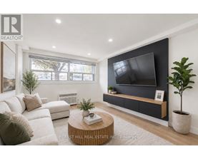 A modern living room with a white sofa, a wooden coffee table, and a flat-screen TV mounted on the wall.