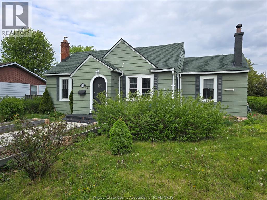 A green house with a grey roof and a chimney is surrounded by greenery.